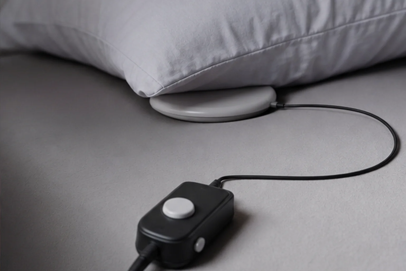 Wired bed-shaker puck placed beneath the edge of a pillow