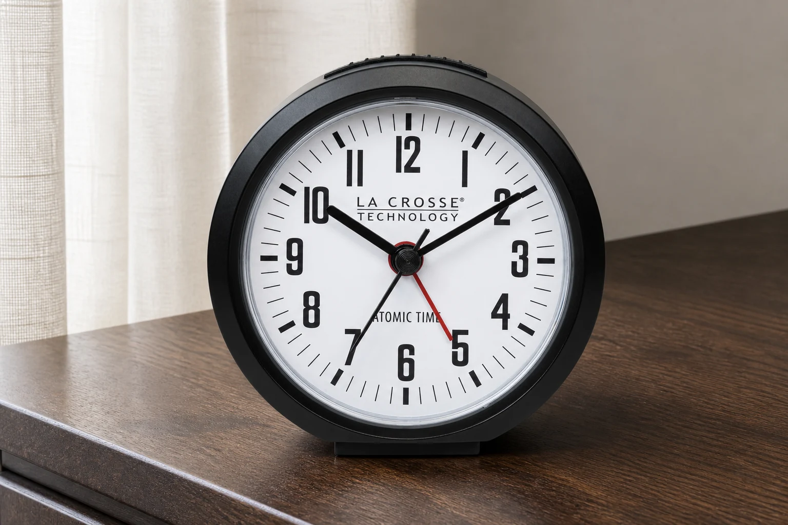La Crosse 617-710B with a round dark case, white dial and red alarm hand on walnut beside a curtain